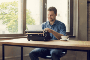 An American writing a story in a typewriter. There is a a cup of cofee on the table